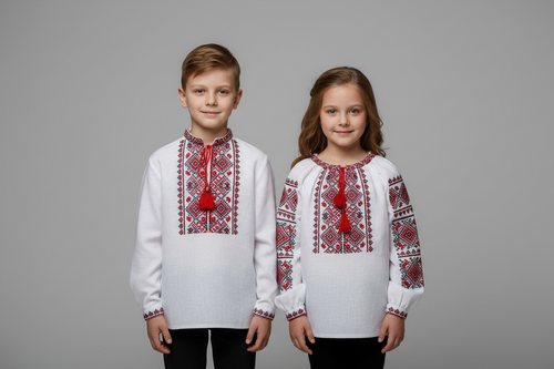 A boy and a girl in traditional white Ukrainian vyshyvanka with red and black geometric embroidery, photographed in a studio setting.